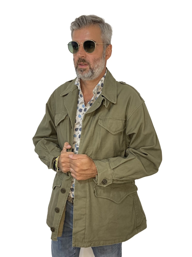 May include: A green field jacket with a button closure and multiple pockets. The jacket has a relaxed fit and is made of a durable fabric.