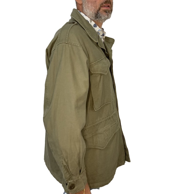 May include: A green field jacket with a button-up front and multiple pockets. The jacket is made of a durable cotton fabric.