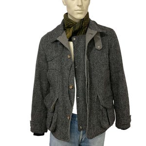 May include: A gray herringbone jacket with a gray collar and pockets, displayed on a mannequin. The jacket has brown buttons and is paired with a green and black scarf and blue jeans.