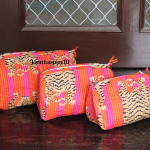 May include: Three pink and orange striped fabric cosmetic bags with a tiger print. The bags are lined up in a row from largest to smallest.