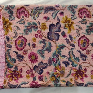 Op de afbeelding: Een roze kantha-deken met een bloemenpatroon in tinten roze, paars, groen en goud. De deken is met de hand gestikt en heeft een traditioneel Indiaas ontwerp.