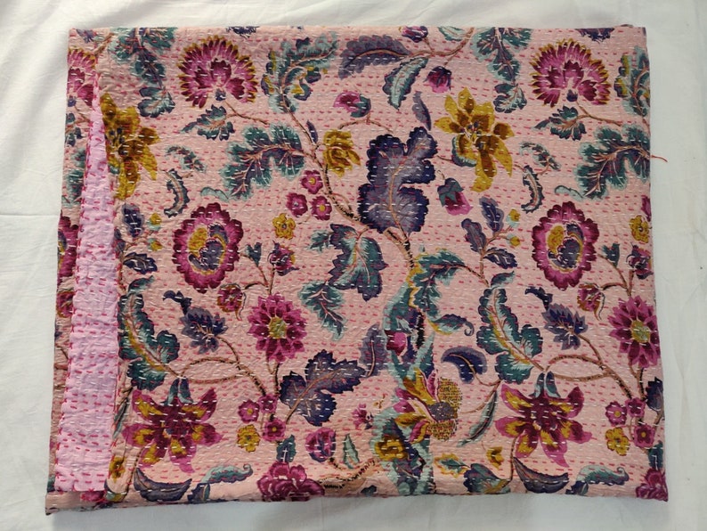 Op de afbeelding: Een roze kantha-deken met een bloemenpatroon in tinten roze, paars, groen en goud. De deken is met de hand gestikt en heeft een traditioneel Indiaas ontwerp.
