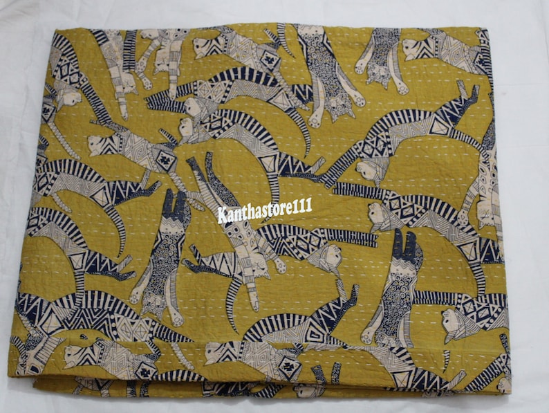 May include: A yellow kantha quilt with a pattern of black and white cats. The cats are in various poses and are outlined in black. The quilt is made of cotton and is hand-stitched.