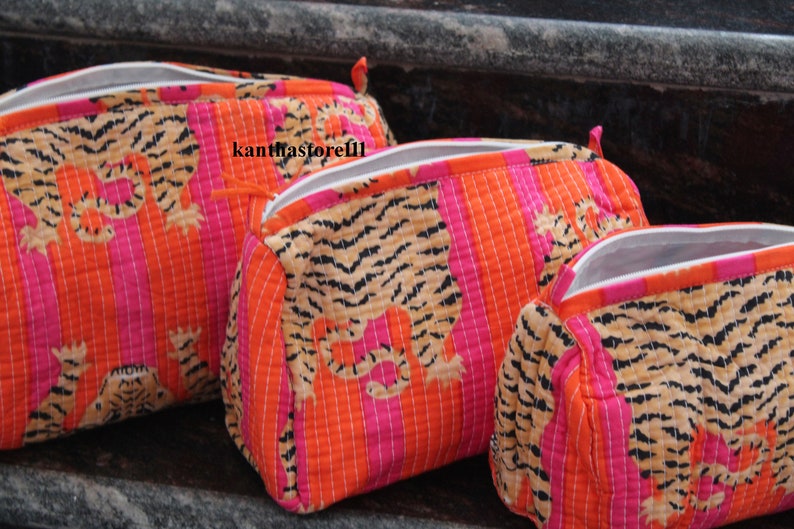 May include: Three zippered pouches with a tiger print design. The pouches are made of a quilted fabric with orange and pink stripes. The pouches are lined with white fabric.