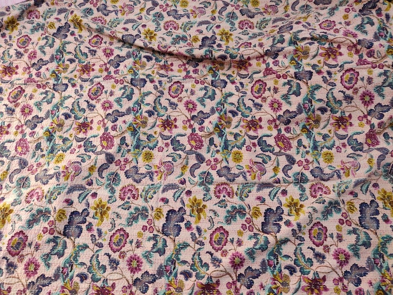 Op de afbeelding: Een cr&egrave;mekleurige stof met een bloemenpatroon in tinten roze, blauw en geel. De stof heeft een gestikte textuur.