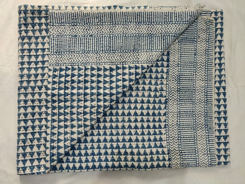 May include: A blue and white kantha quilt with a geometric pattern. The quilt is folded in half and has a textured surface.