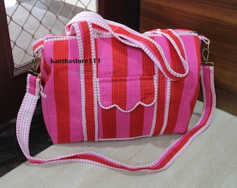 May include: A pink and red striped tote bag with a matching shoulder strap. The bag features a scalloped pocket and the text "kanthastore111". The bag has a white trim and gold-colored hardware.