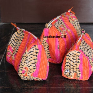 May include: Three quilted makeup bags with a tiger print design. The bags are pink, orange, and brown with a white zipper. The bags are lined up in a row from largest to smallest.