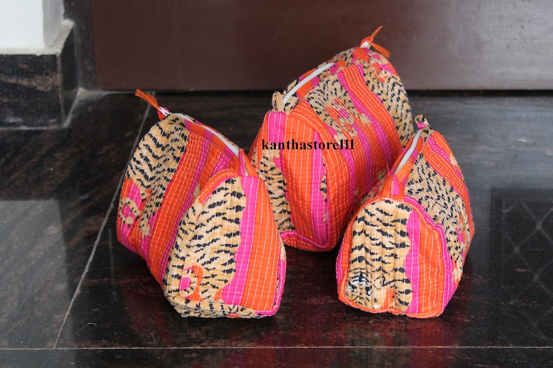 May include: Three quilted makeup bags with a tiger print design. The bags are pink, orange, and brown with a white zipper. The bags are lined up in a row from largest to smallest.