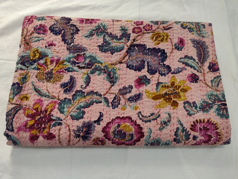 Op de afbeelding: Roze kantha-deken met een bloemenpatroon in tinten paars, groen en geel. De deken is gemaakt van katoen en heeft een handgestikt ontwerp.