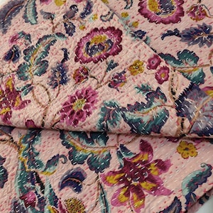 Op de afbeelding: Een roze kantha-deken met een bloemenpatroon in tinten roze, paars, groen en geel. De deken is gemaakt van katoen en heeft een handgestikt ontwerp.