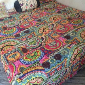 May include: A colorful kantha quilt with a geometric pattern in shades of pink, blue, green, yellow, and brown. The quilt is made of recycled saris and is hand-stitched.