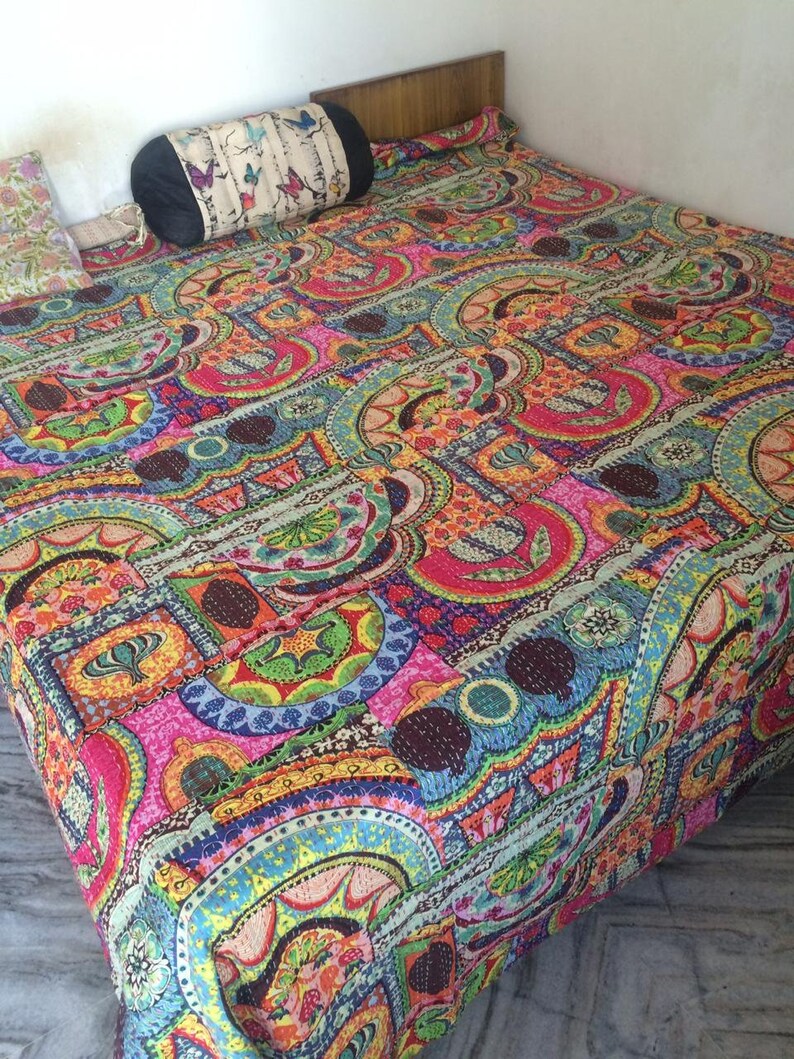 May include: A colorful kantha quilt with a geometric pattern in shades of pink, blue, green, yellow, and brown. The quilt is made of recycled saris and is hand-stitched.