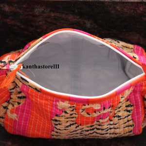 May include: A bright orange, pink and brown quilted makeup bag with a zipper closure and a tassel pull. The bag is open and the inside is lined with a light grey fabric.