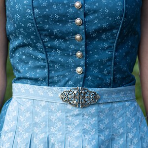 Puede incluir: Un vestido tradicional b&aacute;varo azul y blanco con una hebilla plateada. El corpi&ntilde;o es azul oscuro con un estampado floral y botones plateados. La falda es azul claro con un estampado floral blanco.