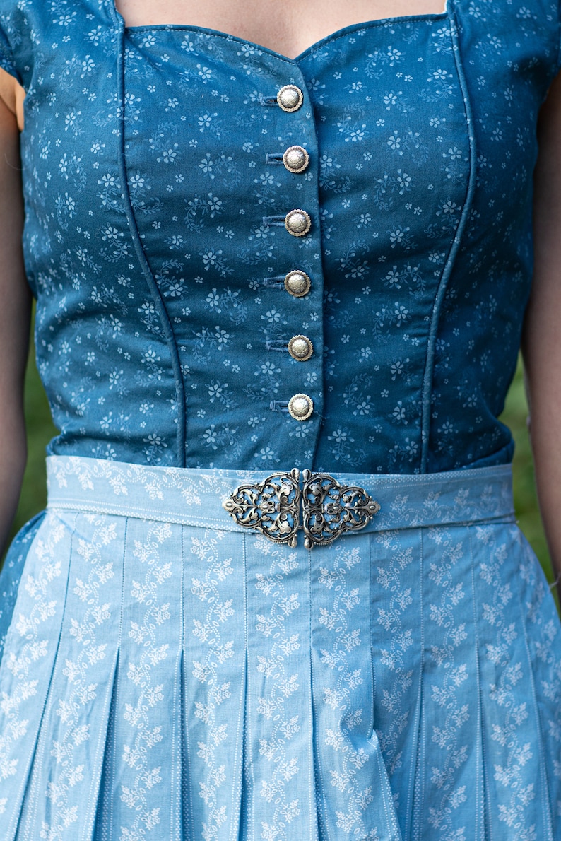 Puede incluir: Un vestido tradicional b&aacute;varo azul y blanco con una hebilla plateada. El corpi&ntilde;o es azul oscuro con un estampado floral y botones plateados. La falda es azul claro con un estampado floral blanco.