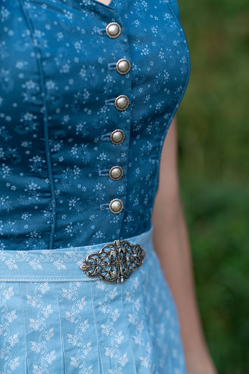 Puede incluir: Un vestido tradicional b&aacute;varo azul y blanco con una hebilla plateada y botones plateados. El corpi&ntilde;o es azul oscuro con un estampado floral y la falda es azul claro con un estampado floral blanco.