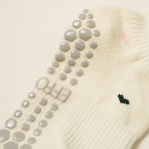 May include: Cream-colored sock with gray non-slip grips on the sole. The sock features the word "EFFO" printed in gray and a small green heart design. Pink accents are also visible.