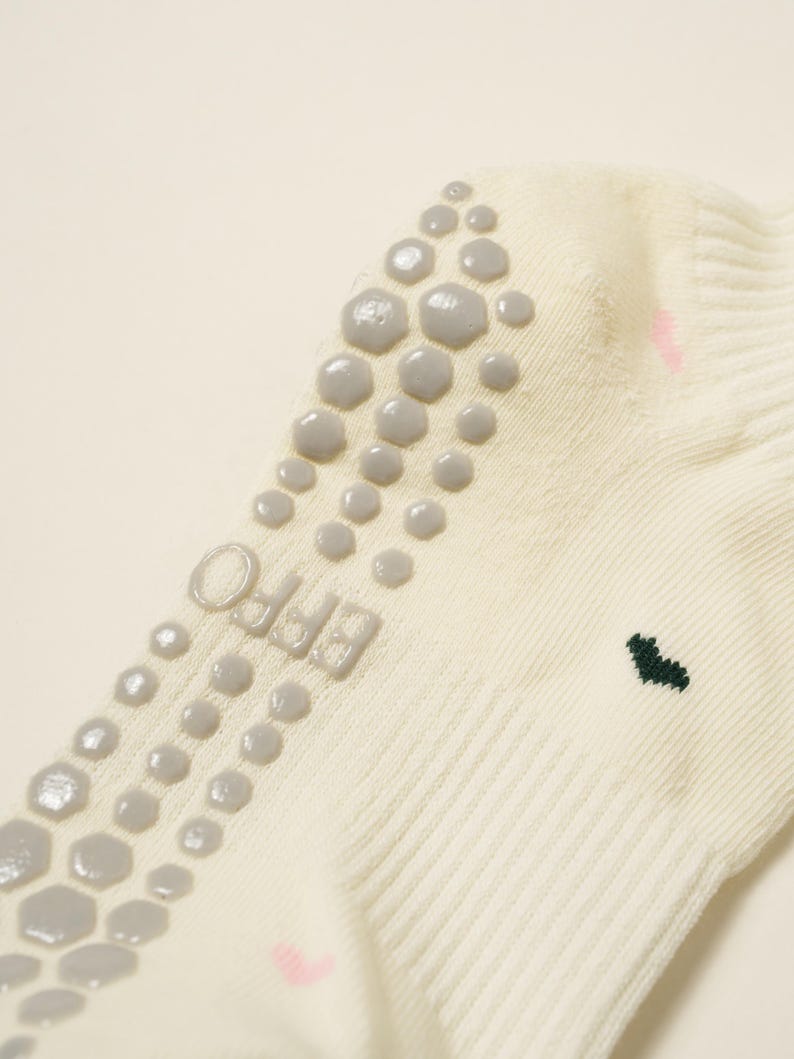 May include: Cream-colored sock with gray non-slip grips on the sole. The sock features the word "EFFO" printed in gray and a small green heart design. Pink accents are also visible.