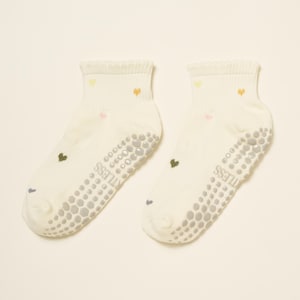 May include: A pair of off-white ankle socks with small, colorful heart designs. The socks have a textured, non-slip grip on the soles and the word "STITLESS" printed on the side. The hearts are in shades of yellow, pink, and orange.