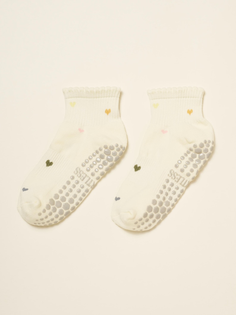May include: A pair of off-white ankle socks with small, colorful heart designs. The socks have a textured, non-slip grip on the soles and the word "STITLESS" printed on the side. The hearts are in shades of yellow, pink, and orange.