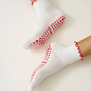 May include: White socks with red wavy trim and red dotted grips on the soles. The word "EFFORTLESS" is printed in red on the sole of each sock. The socks are ribbed and appear to be made of a soft material.