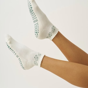 May include: White socks with green non-slip dots on the soles and the word "ORTLESS" printed on the side. The cuffs feature a green floral design. These socks are designed for comfort and grip.