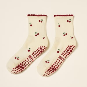 Peut inclure: Une paire de chaussettes cr&egrave;me avec un motif de cerises. Les chaussettes ont un bord festonn&eacute; et une adh&eacute;rence antid&eacute;rapante rouge sur les semelles. Les cerises sont rouges avec des tiges vertes.