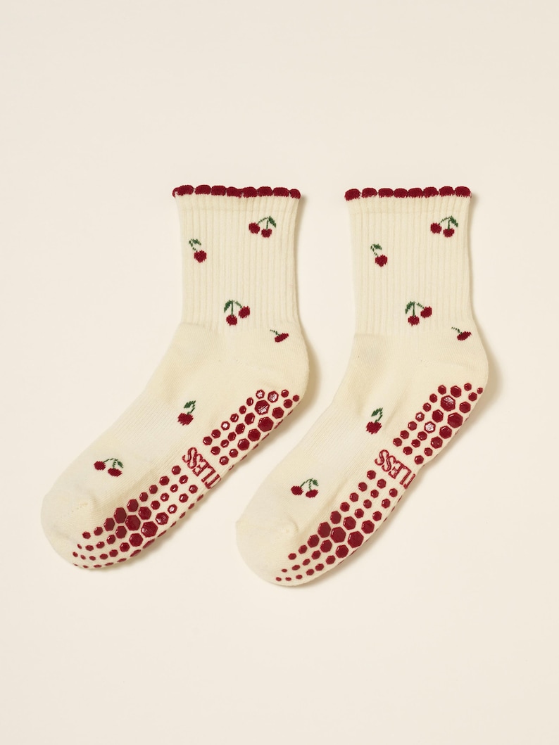 Peut inclure: Une paire de chaussettes cr&egrave;me avec un motif de cerises. Les chaussettes ont un bord festonn&eacute; et une adh&eacute;rence antid&eacute;rapante rouge sur les semelles. Les cerises sont rouges avec des tiges vertes.