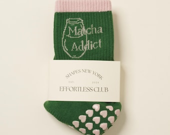 Puede incluir: Calcetines verdes con una banda rosa en la parte superior y corazones rosas en la parte inferior. Los calcetines tienen el texto "Matcha Addict" en la parte delantera. Los calcetines están empaquetados con una etiqueta blanca que dice "Shapes New York Est. 2024 Effortless Club".