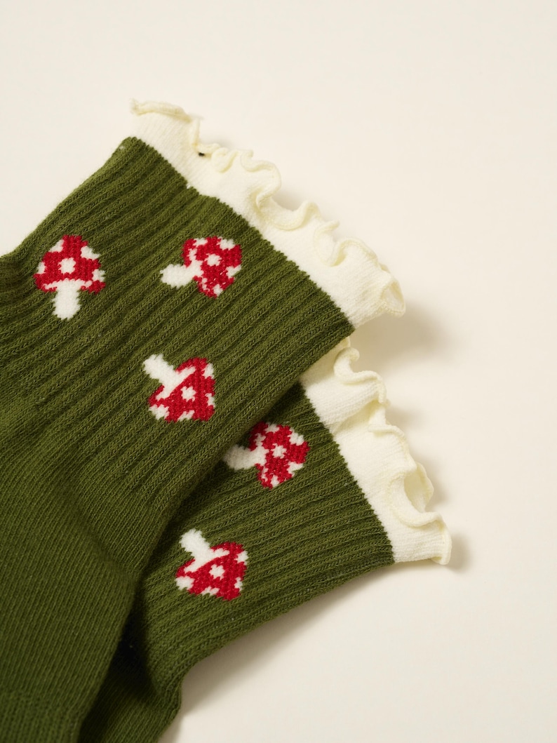 May include: A pair of green socks with a ribbed texture, featuring a pattern of red and white mushroom designs. The socks have a white ruffled trim at the top.