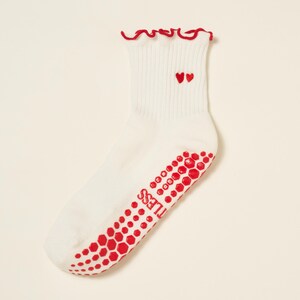 May include: White ankle socks with red accents. The socks feature a red ruffled trim at the top and two embroidered red hearts. The soles have a red, honeycomb-patterned grip with the word "TILESS" printed on the side.