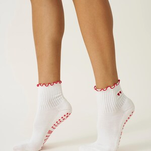 May include: White ankle socks with a red scalloped trim and red non-slip grips on the soles. The socks have a ribbed design and a small red heart detail near the ankle.