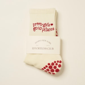 May include: White socks with red grip dots on the bottom and the text "pretty girls go to pilates" in red with a small red heart.