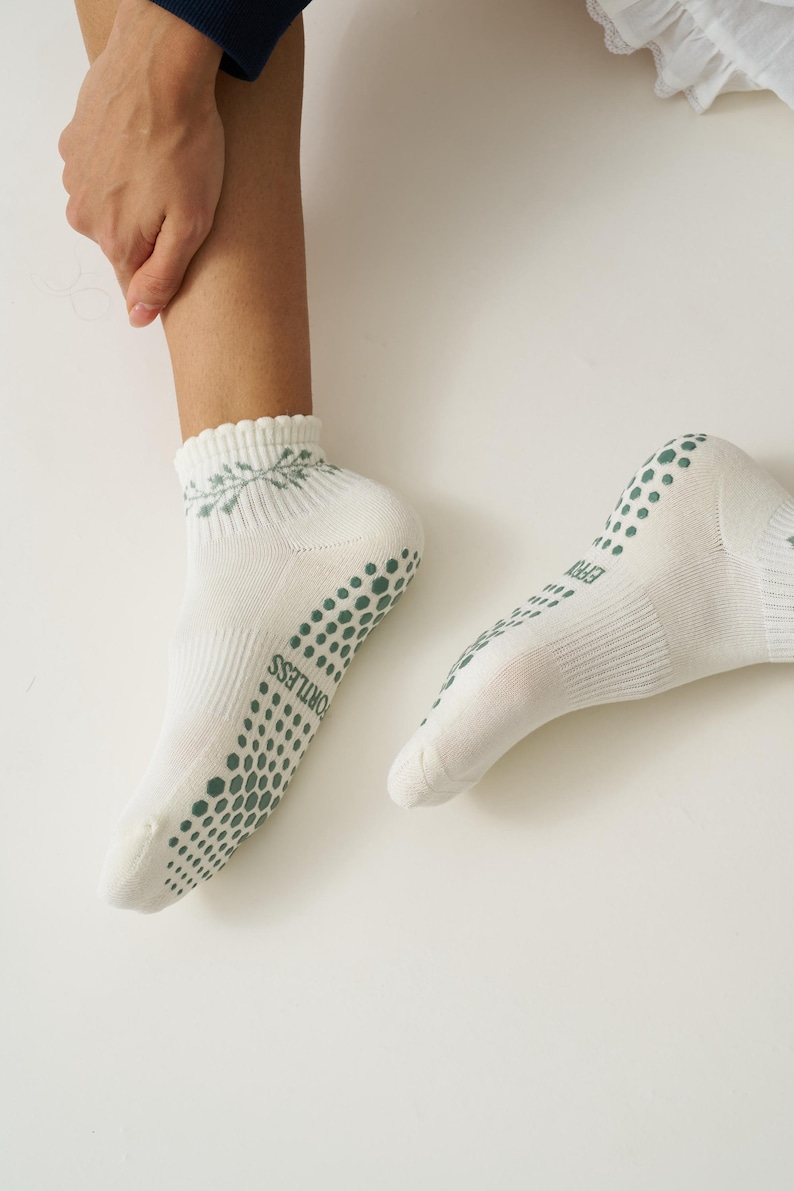 May include: White ankle socks with green non-slip dots on the soles and heels. The socks have a decorative floral pattern at the cuff and the word "FORTLESS" printed on the side. The socks are designed for comfort and grip.