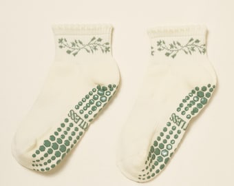 May include: A pair of off-white ankle socks with a floral design in sage green at the cuff. The soles feature a pattern of green hexagonal grips and the word "LESS". These socks are designed for comfort and grip.