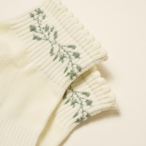 May include: A pair of cream-coloured socks with a ribbed cuff. The cuff features a delicate green floral pattern. The socks are made of a soft, textured material, and the design is simple and elegant.