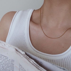 Puede incluir: Primer plano de una persona que lleva un top blanco de tirantes y una fina cadena de oro.