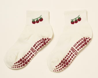 May include: A pair of white ankle socks with a red and green embroidered raspberry design near the top. The soles have a maroon, non-slip grip pattern with the word "LESS" printed on them.