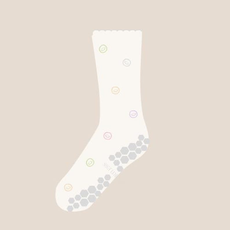 May include: A white sock with a scalloped top edge and a pattern of colorful smiley faces. The sole features a gray, honeycomb-patterned grip. The sock is designed for comfort and style.