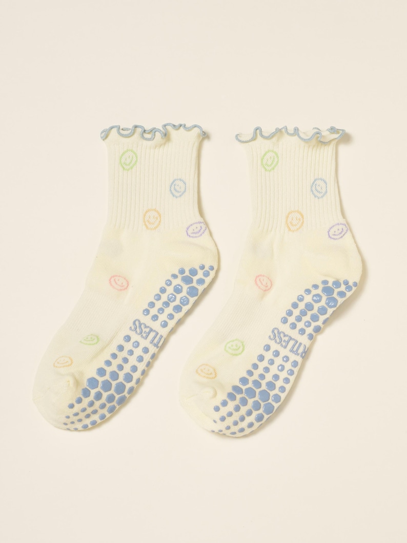 May include: A pair of off-white socks with a light blue ruffled trim and a pattern of colorful smiley faces. The soles have blue non-slip grips with the word "TUTLESS" printed on them.