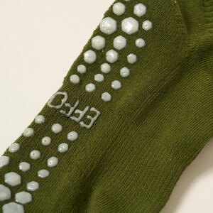 May include: Close-up of an olive green sock with white, textured, non-slip grips. The word "EFFO" is printed in white on the side of the sock. The grips are arranged in a pattern along the top and side of the sock.