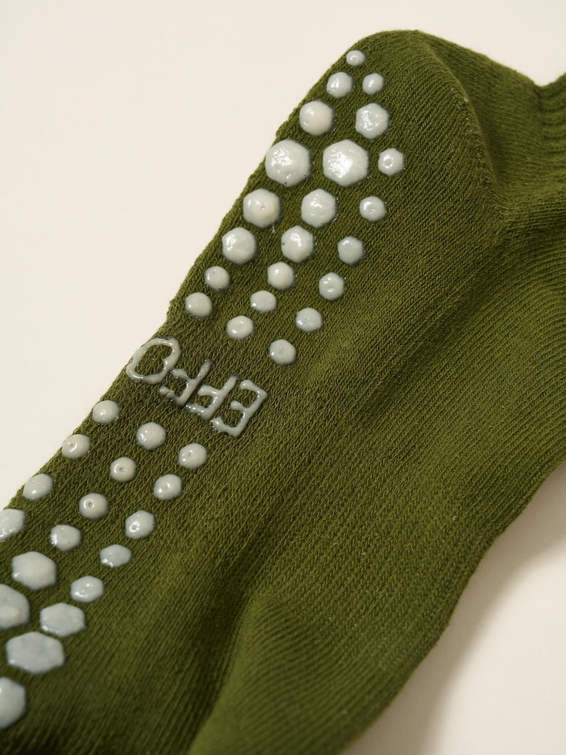 May include: Close-up of an olive green sock with white, textured, non-slip grips. The word "EFFO" is printed in white on the side of the sock. The grips are arranged in a pattern along the top and side of the sock.