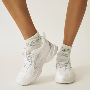 May include: White trainers with a chunky sole and mesh detailing. The shoes are paired with white socks featuring a green floral pattern. The trainers have the brand name "Li-Ning" on the tongue.
