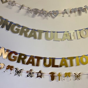 May include: Two gold foil banners spelling "Congratulations" with blue string and white string with various gold and silver decorative accents.