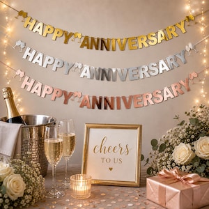 May include: Three metallic banners that read "Happy Anniversary" hang above a table setting. A gold-framed sign says "Cheers to Us." A champagne bottle sits in an ice bucket, with two champagne flutes. A gift box and flowers complete the celebratory scene.