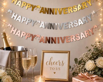 May include: Three metallic banners that read "Happy Anniversary" hang above a table setting. A gold-framed sign says "Cheers to Us." A champagne bottle sits in an ice bucket, with two champagne flutes. A gift box and flowers complete the celebratory scene.