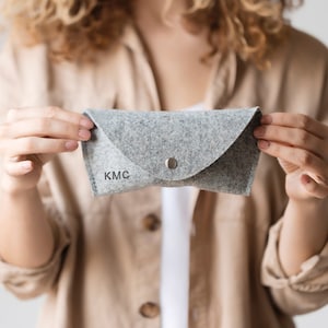 May include: A gray felt glasses case with a silver button closure and the initials "KMC" embroidered on the front.
