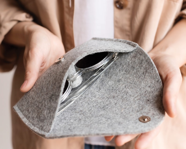May include: A gray felt sunglasses case with a zipper closure. The case is open and a pair of sunglasses is inside.