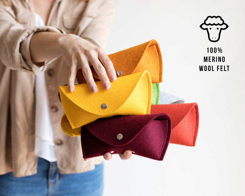 May include: A set of five colorful felt pouches, each with a button closure. The pouches are stacked in a rainbow order, from orange to red. The pouches are made of 100% merino wool felt.